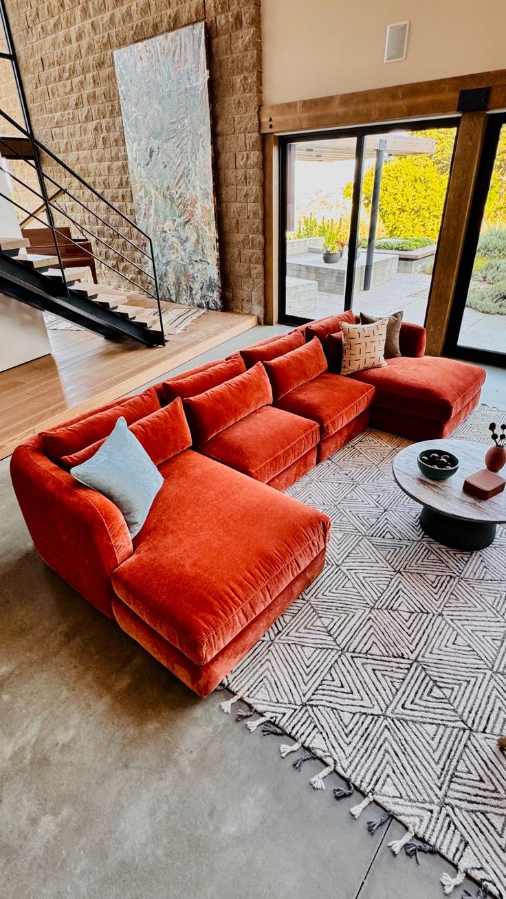 a living room filled with red couches next to a stair case and large windows