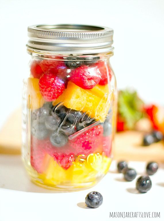 a mason jar filled with fresh fruit and berries on top of a table next to a cutting board