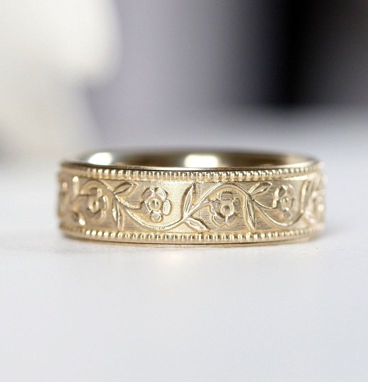 a gold wedding band with an intricate design on the outside and inside, sitting on a white surface