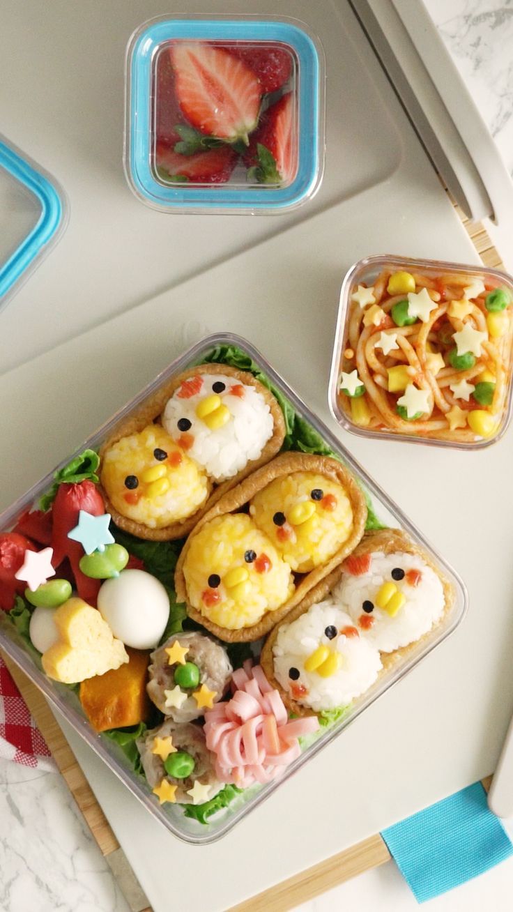 two plastic containers filled with food on top of a table next to strawberries and other items