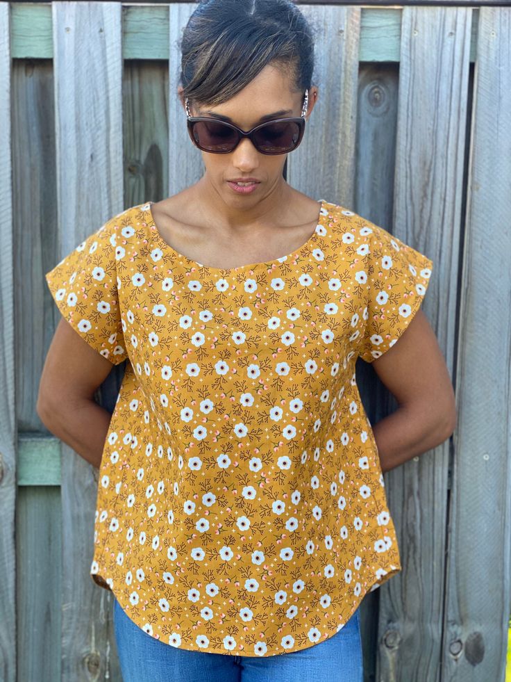 "Beautiful \"Spring\" ladies top featuring a boat neckline with a boxy type of fit.  This top has a curved hem and the back is slightly longer, it also has a pleat and a matching back yoke.   Fits well with jeans or tucked in to a skirt. This is the wardrobe essential! Choice number 1 features a mustard background with cream flowers and a cream back yoke. But there are many fabrics to choose from. Made from 100% cotton.  Sizes: - XS - S - M - L - XL - 2XL Please advise which size you would like on check out. * Please note that items are made to order and picture placement may vary from item to item. * Please choose your size carefully as refunds will NOT be given on made to order items. Pattern used is the Bondi Top by Sew to Grow. Follow us on: Facebook - www.facebook.com/silverthreads IG Tiger Halloween Costume, Ladies Tops Blouses, Trendy Baby Clothes, Harem Shorts, Toddler Romper, Beautiful Shorts, Cream Flowers, Boat Neckline, Boys T Shirts