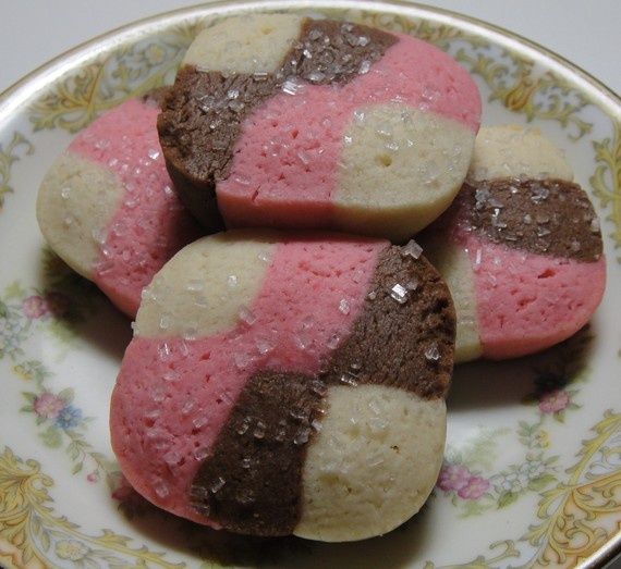 four cookies with pink and white frosting are on a floral plate, sitting on a table