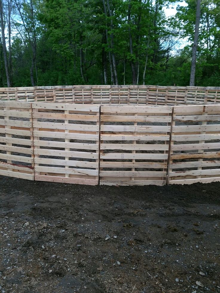 a large wooden fence in the middle of a dirt field with trees in the background