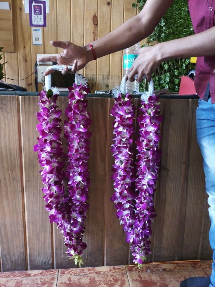 two purple flowers are hanging from the side of a wooden wall and being held by a person