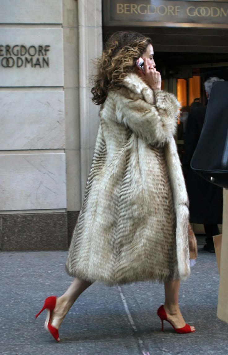 a woman in a fur coat talking on her cell phone while walking down the street