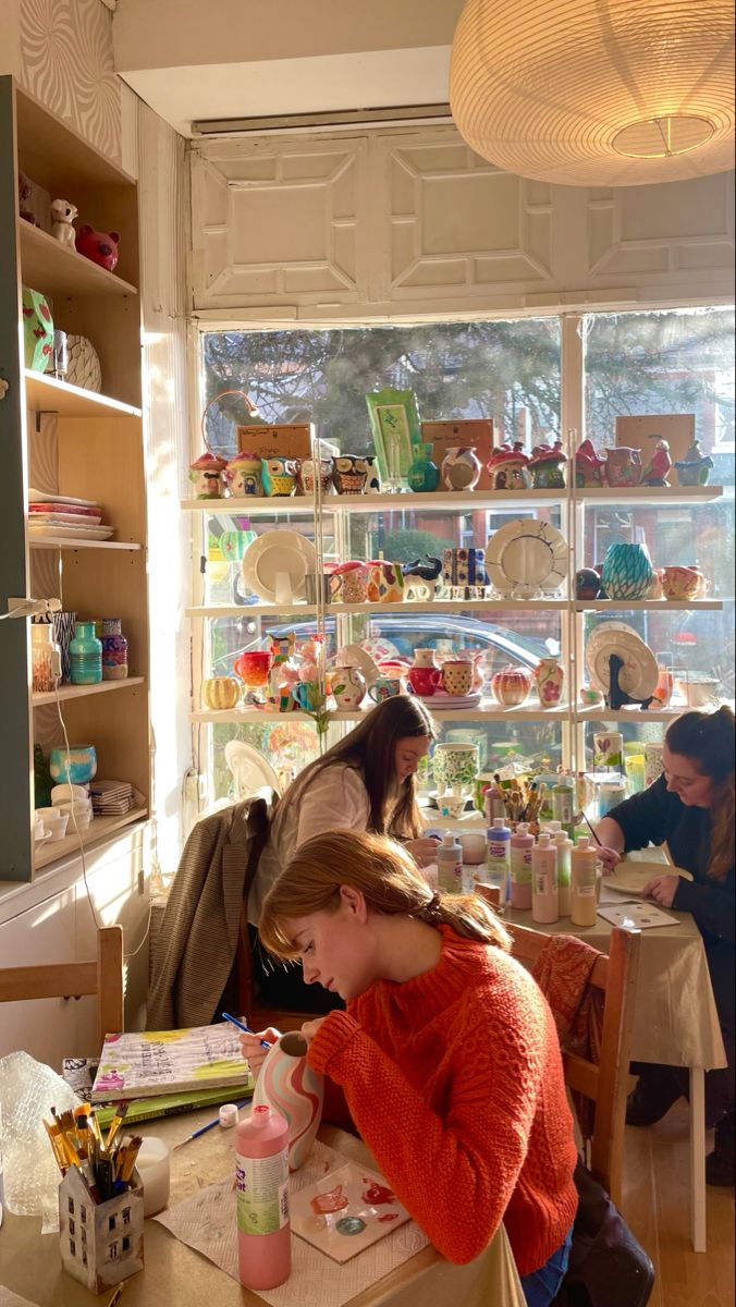 two women sitting at a table in a room with many items on the shelves behind them