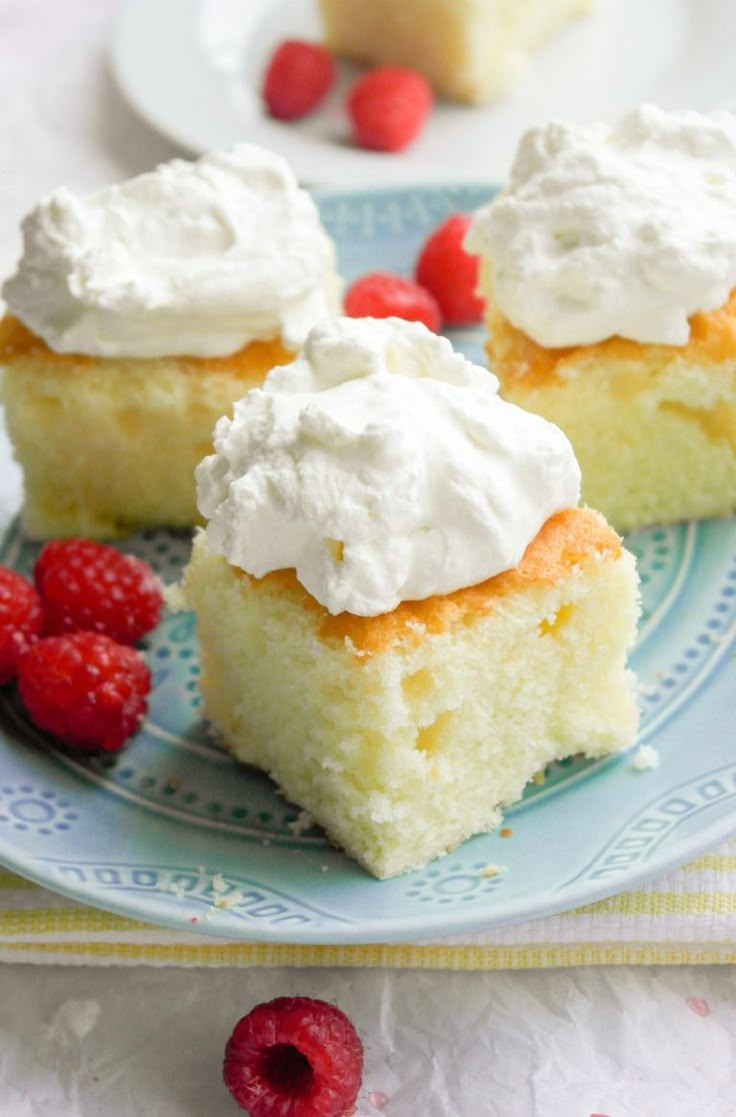 three pieces of cake on a plate with raspberries and whipped cream frosting