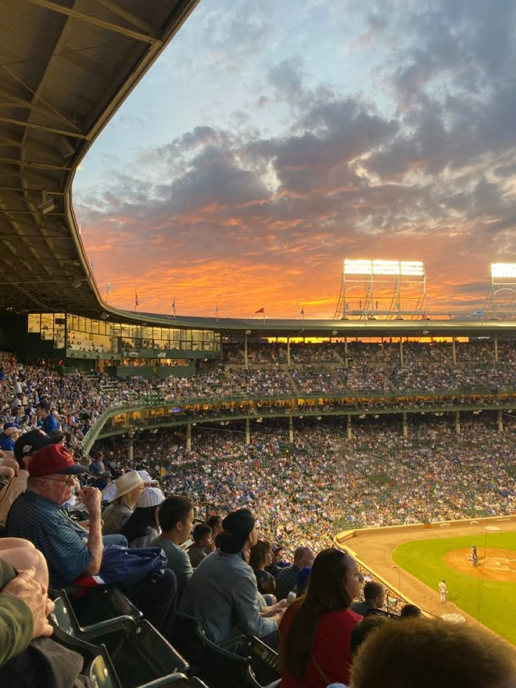 a baseball stadium filled with lots of people sitting in the bleachers at sunset