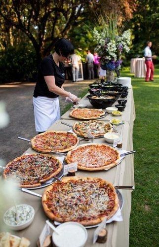 a table topped with lots of pizzas on top of a lush green park covered in trees