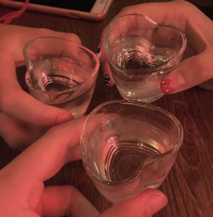 three people holding wine glasses on top of a wooden table with their hands in the air