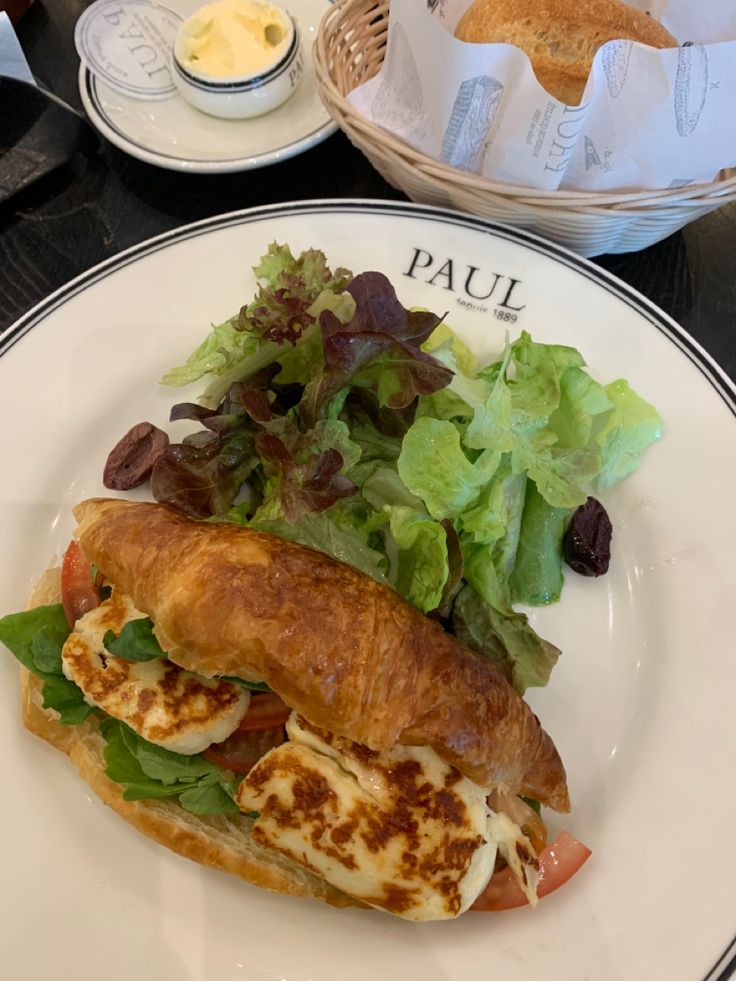 there is a sandwich on the plate with salad and bread in the basket next to it