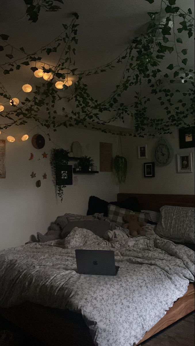 a laptop computer sitting on top of a bed in a room with plants hanging from the ceiling