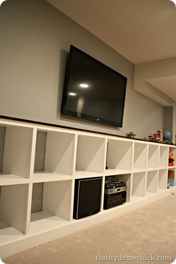 a television mounted on the wall in a living room with white shelving and shelves