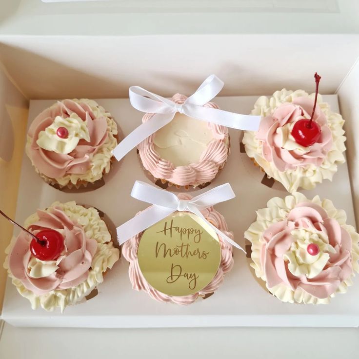 a box filled with cupcakes covered in pink frosting and topped with a cherry