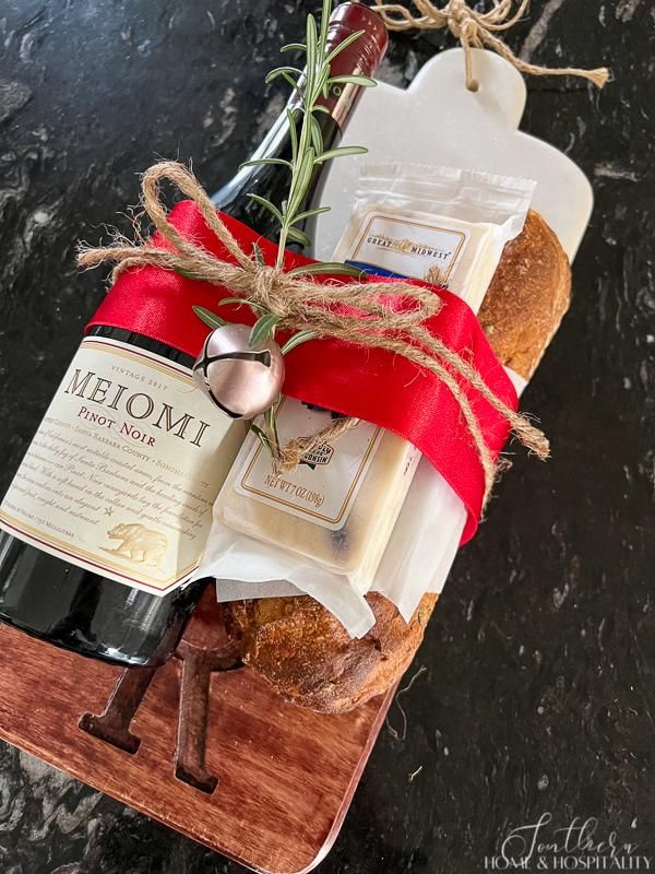 a bottle of wine sitting on top of a cutting board next to bread and cheese