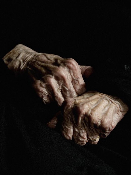 an old woman's hands resting on her lap in the dark, with wrinkles