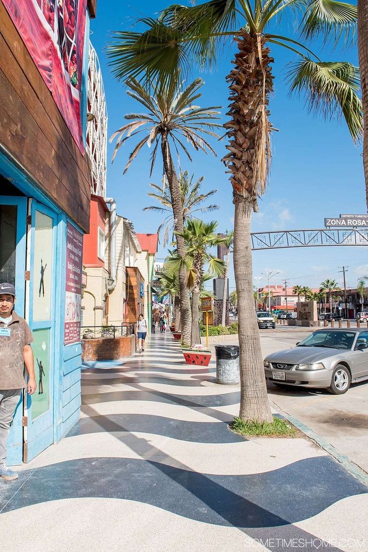 a man is walking down the sidewalk in front of a building with palm trees on both sides