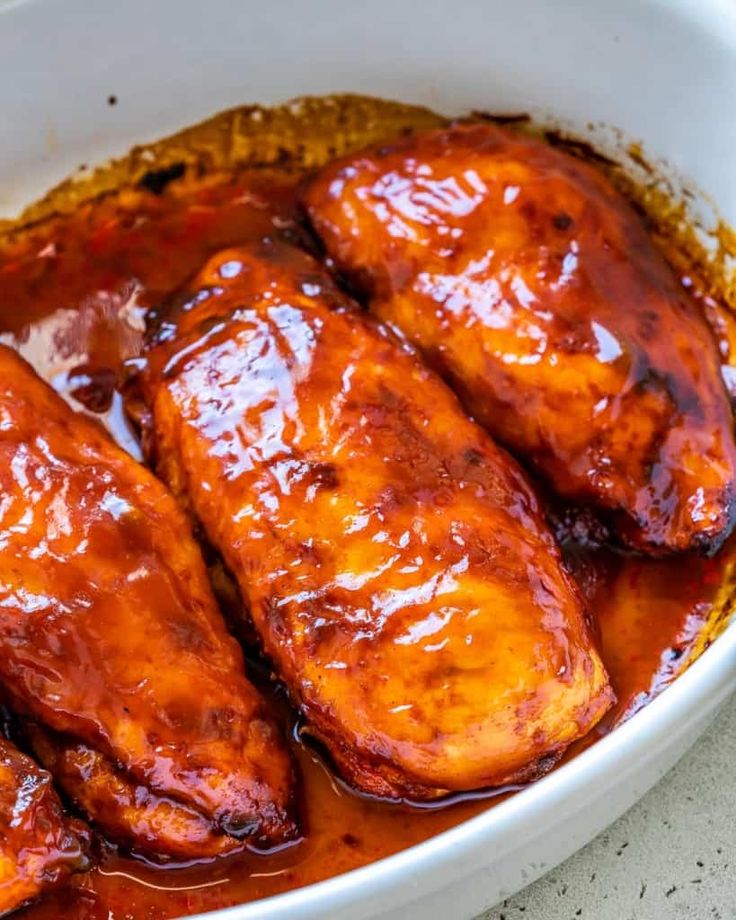 baked bbq chicken breast in a white bowl with sauce on the side and text overlay