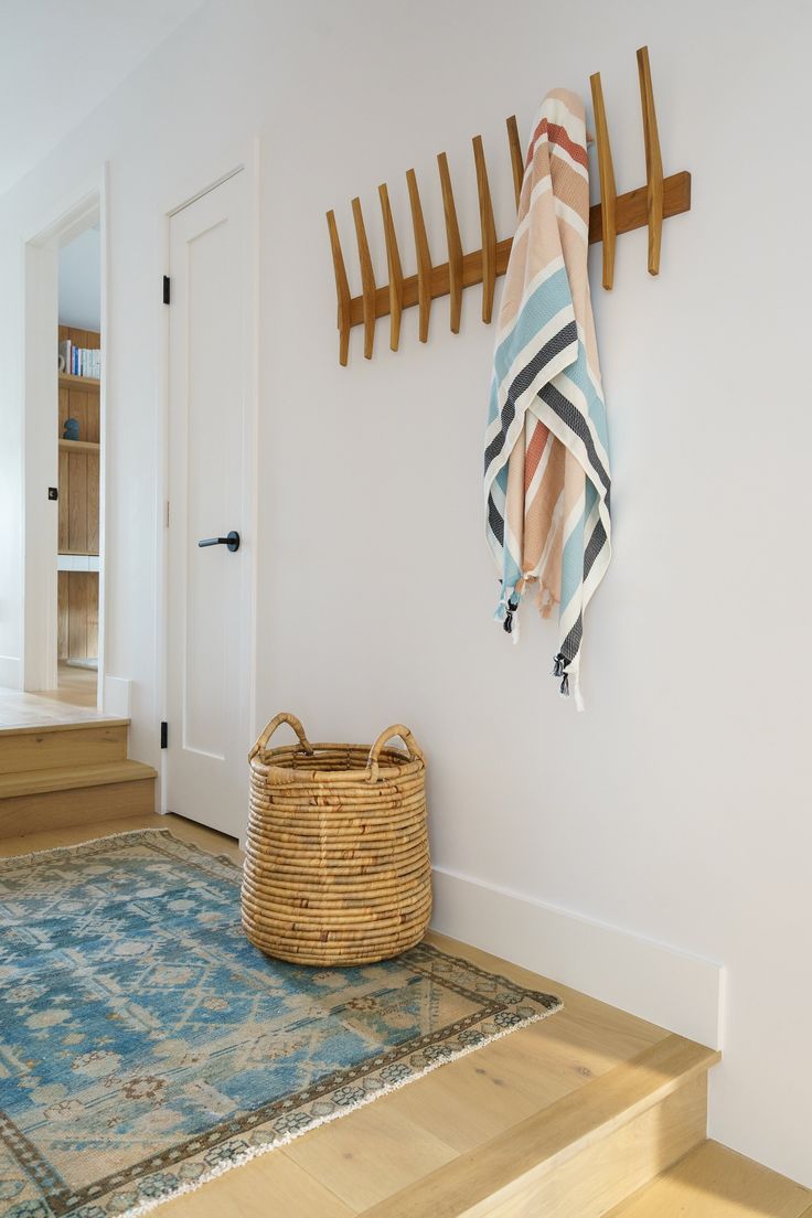 a basket sitting on the floor in front of a wall mounted coat rack with hooks