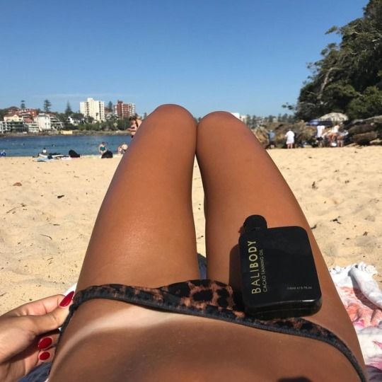 a woman laying on top of a sandy beach next to the ocean with her cell phone