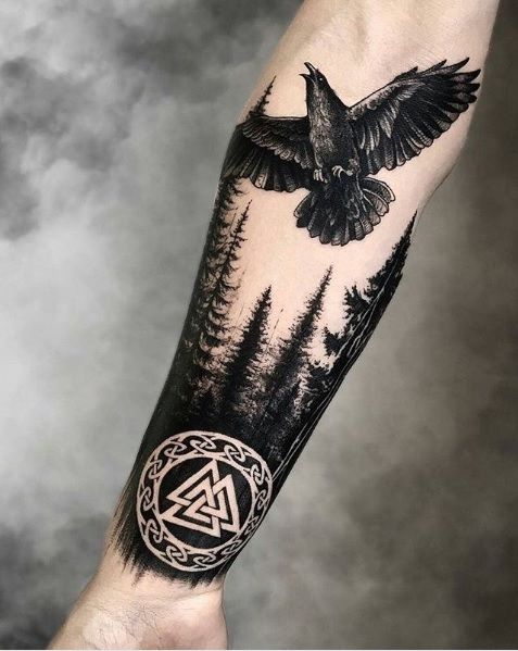 an arm with a bird flying over trees and a triangle tattoo on the left forearm