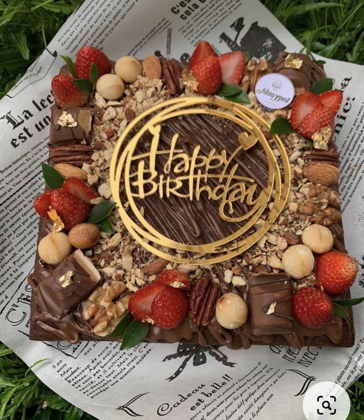 a birthday cake with nuts, chocolate and strawberries on it sitting in the grass