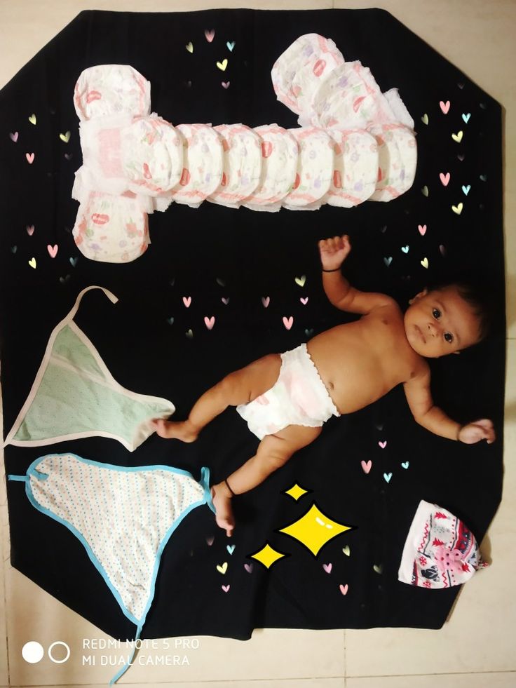 a baby laying on top of a black blanket next to diapers and blankets in the shape of hearts