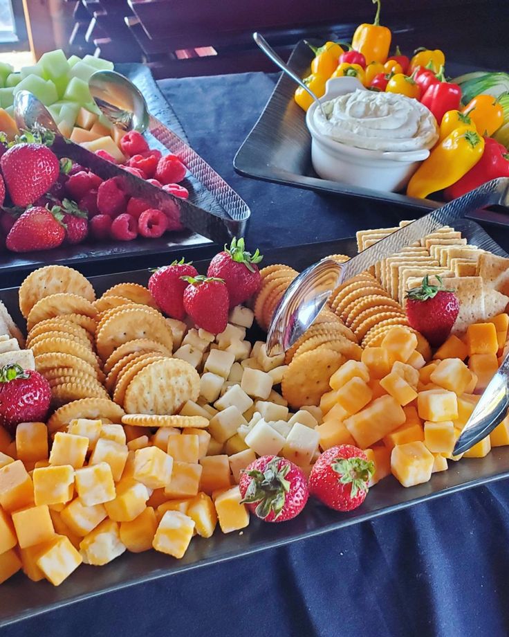 two trays filled with different types of cheese and crackers next to bowls of fruit