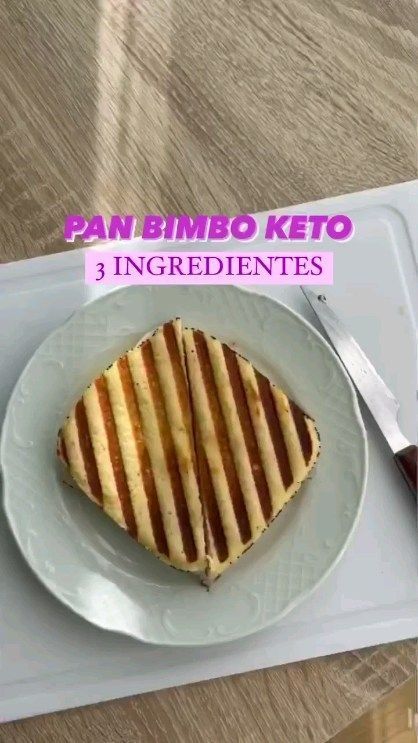 a white plate topped with a sandwich on top of a wooden table next to a knife and fork