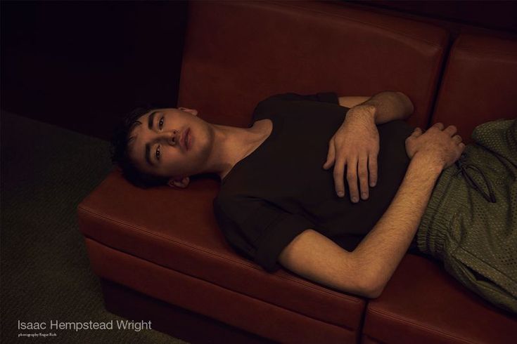 a man laying on top of a red couch next to a green shirt and pillow