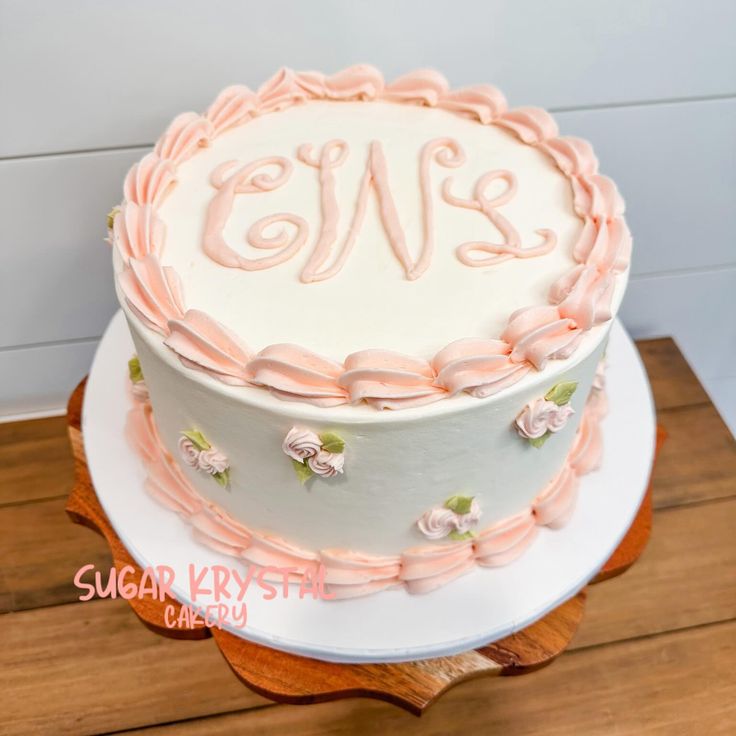 a white cake with pink icing on top of a wooden table next to a wall