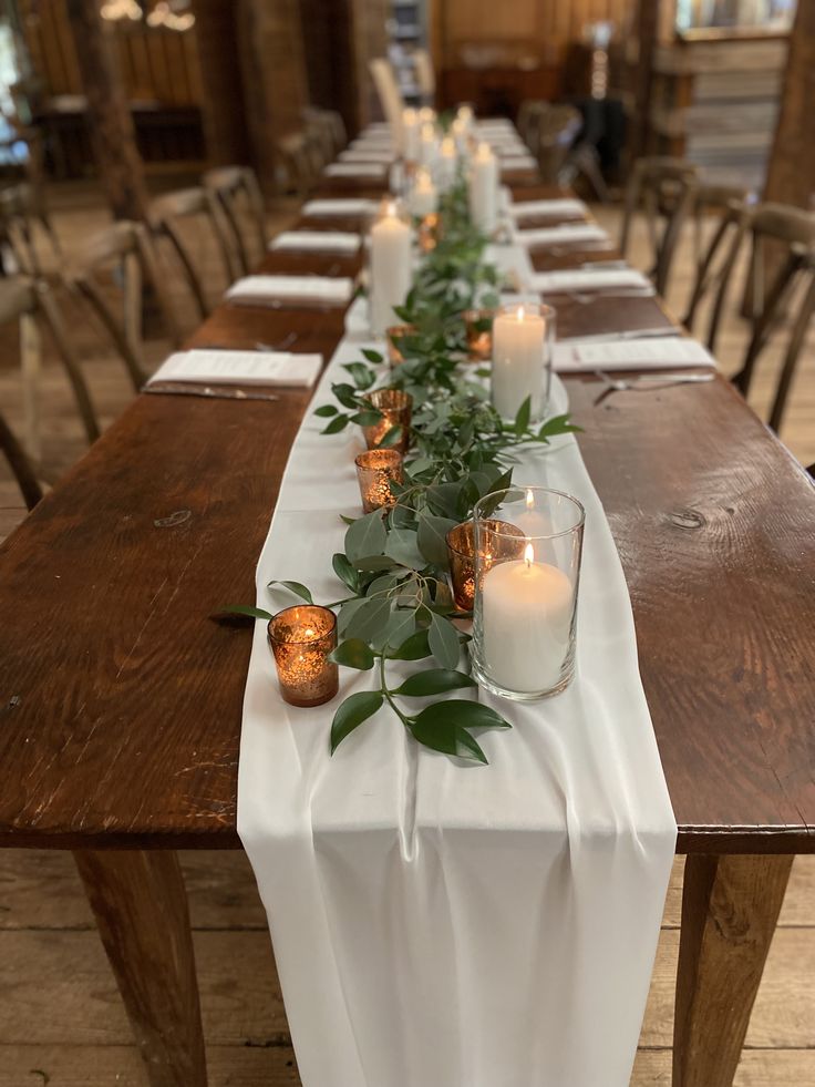 a long table with candles and greenery on it in a room filled with wooden chairs