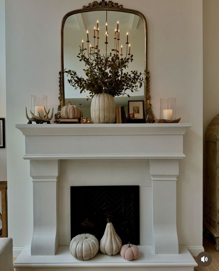 a white fireplace with candles and pumpkins on the mantel in front of it