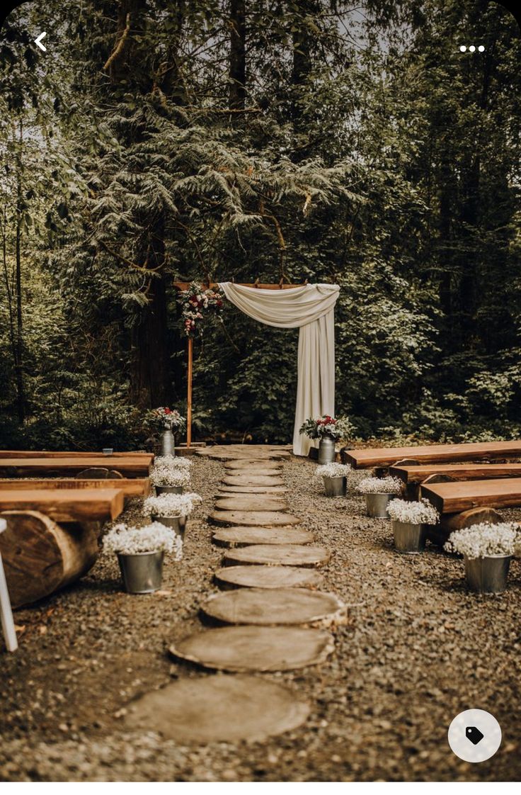 an outdoor ceremony setup with wooden benches and flowers on the aisle, surrounded by greenery