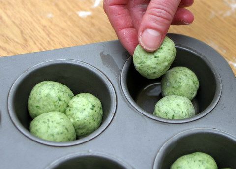 a person placing green balls in a muffin tin with their fingers on the top