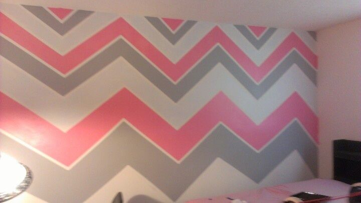 a bed room with a neatly made bed and a large chevron pattern on the wall