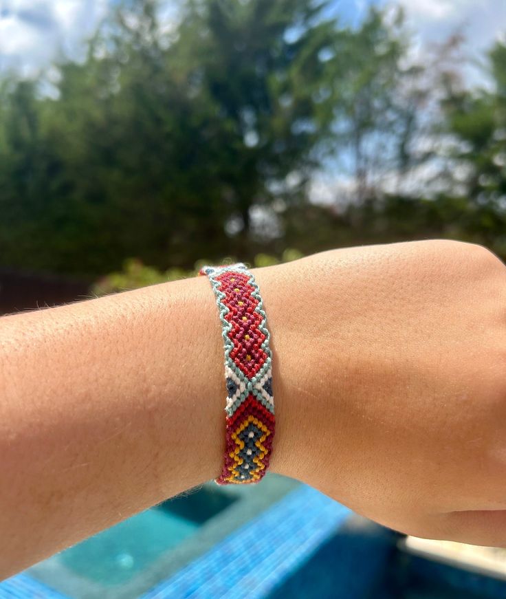 a person's arm with a bracelet on it next to a swimming pool and trees