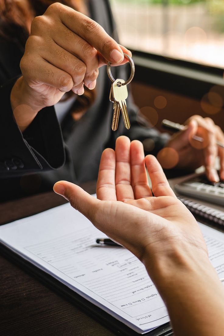 two people holding keys in their hands over a laptop computer and paperwork on the desk