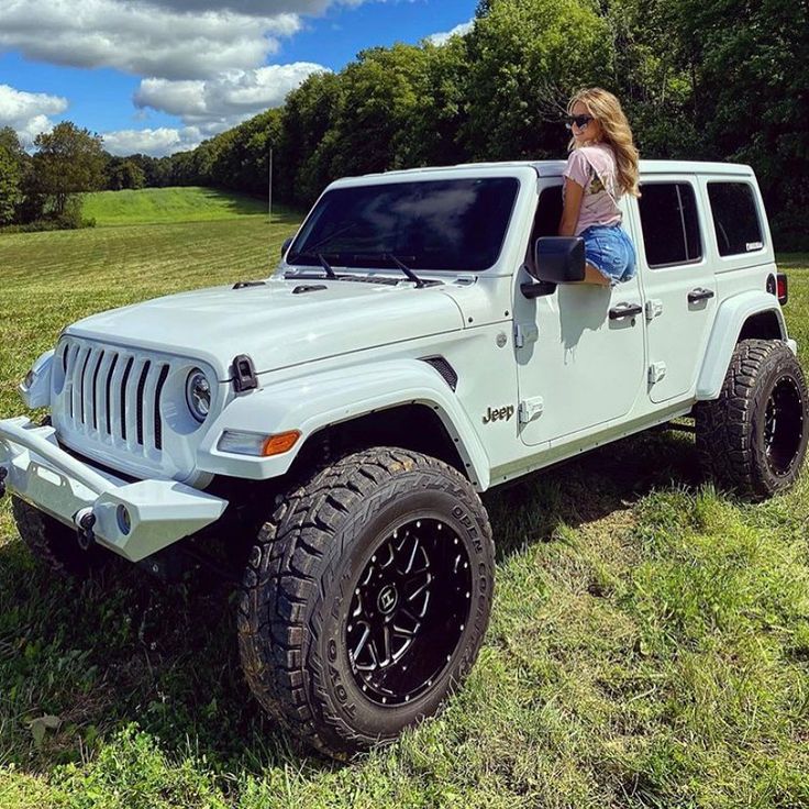 a woman sitting on top of a white jeep in the middle of a grassy field