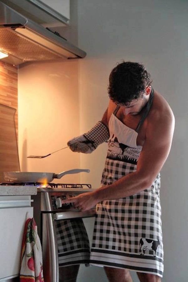 a shirtless man is cooking in the kitchen while wearing an apron and holding a spatula