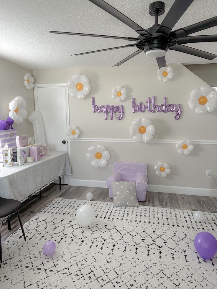 a birthday party with balloons and decorations on the wall, including purple chairs and white tablecloths