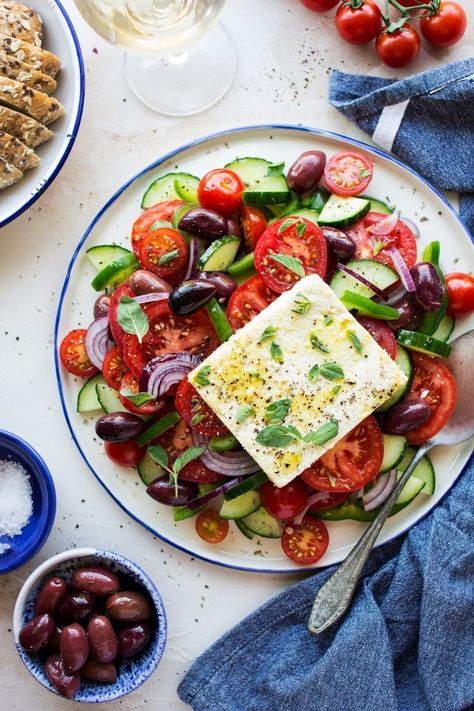 a white plate topped with cucumber, tomatoes and olives next to crackers