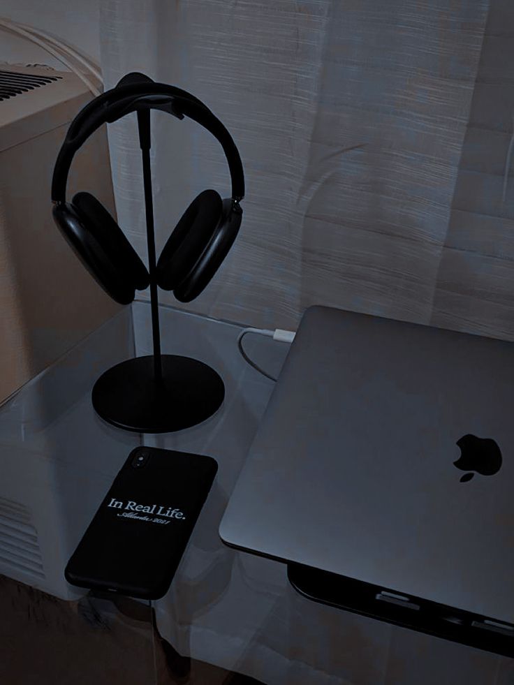 an apple laptop computer sitting on top of a glass table next to headphones and a cell phone