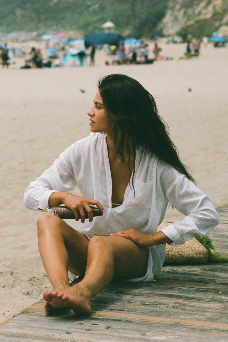 a woman sitting on the beach with her legs crossed