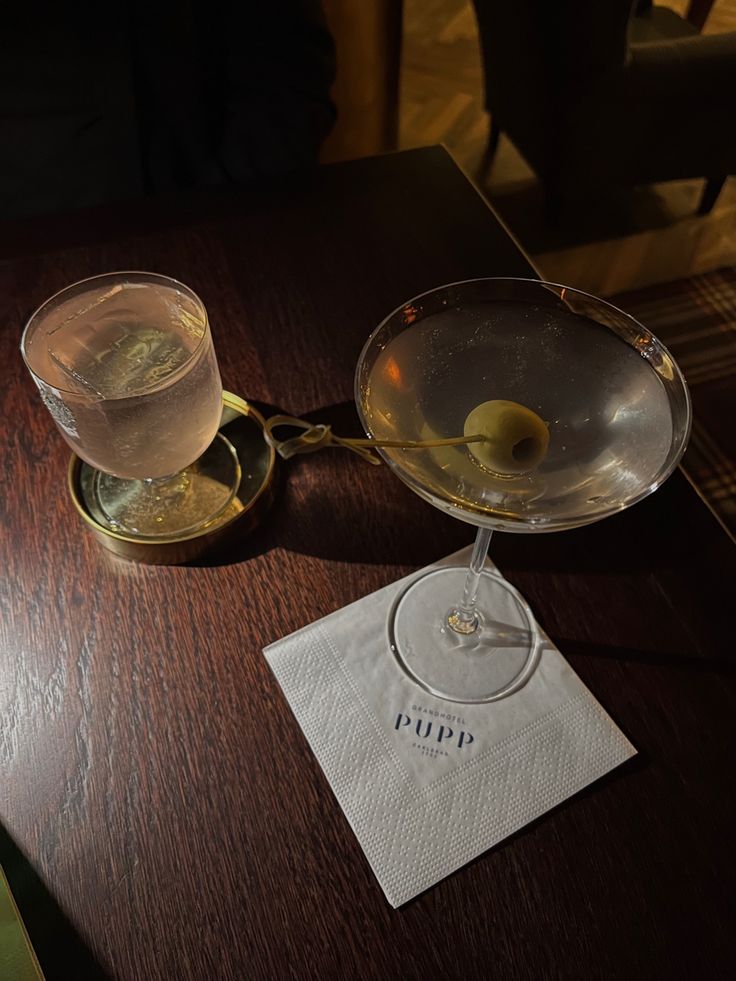 a table topped with two wine glasses filled with liquid and an olive on top of it