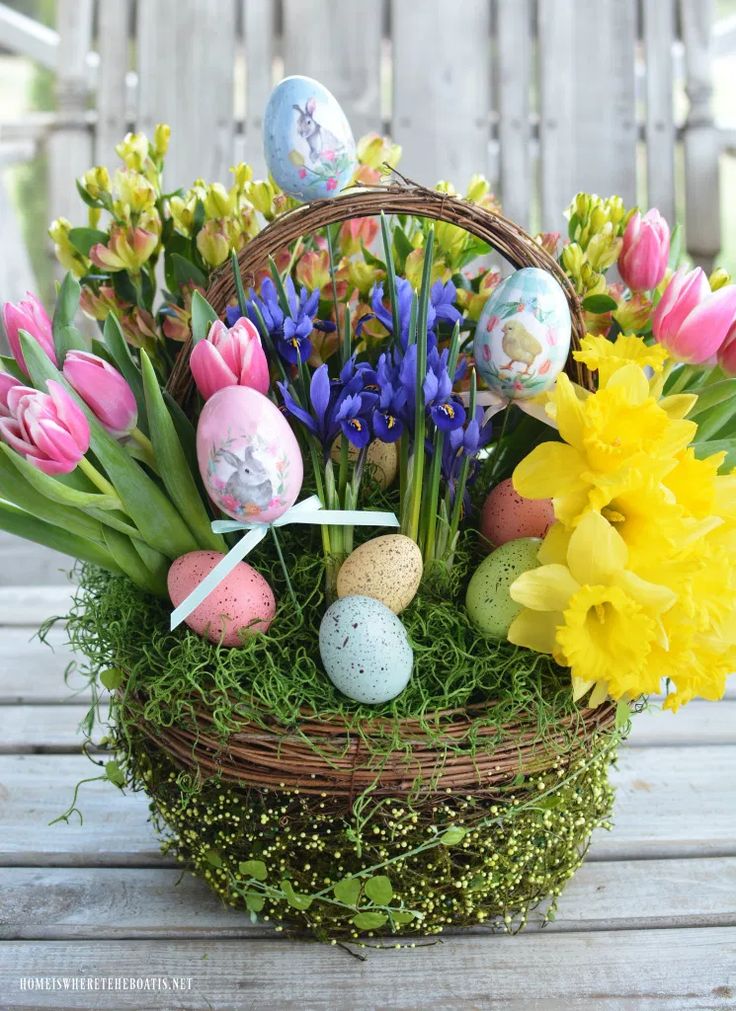 a basket filled with flowers and eggs on top of a wooden table