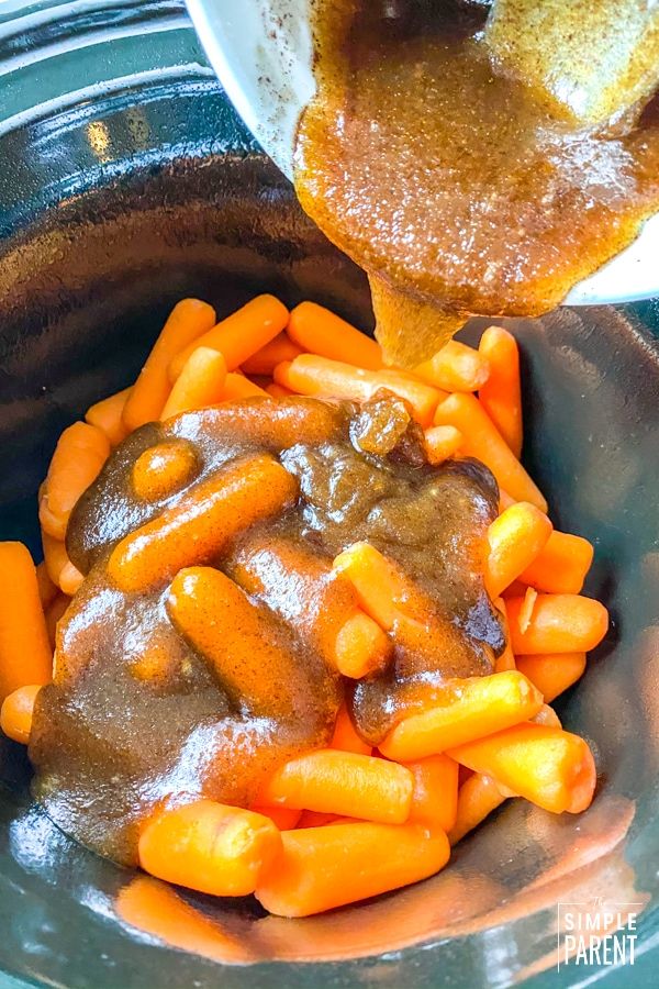 a spoon scooping gravy over some carrots in a crock pot