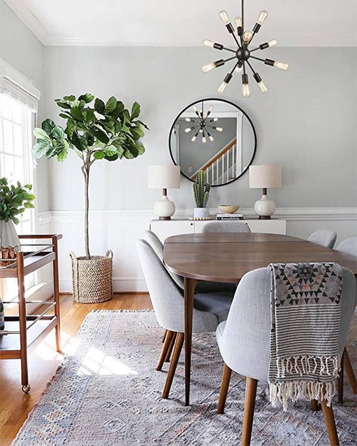 a dining room table and chairs in front of a large mirror with plants on it