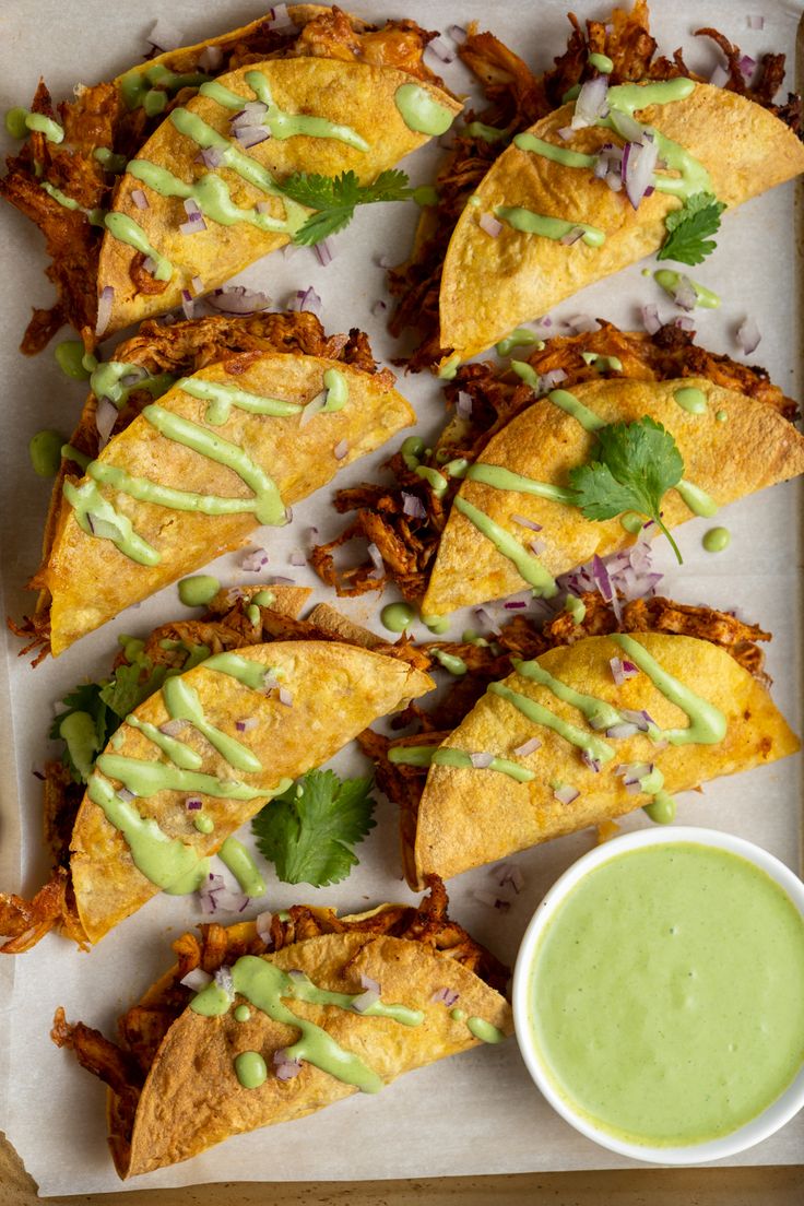 some tacos are sitting on a tray next to a small bowl of green sauce