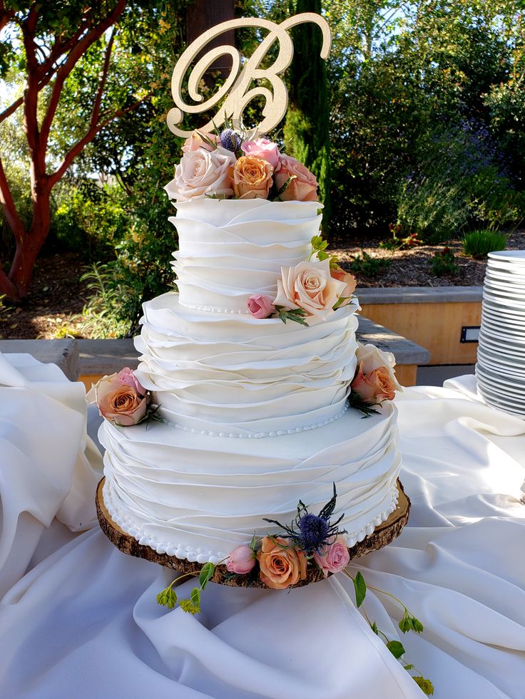 a three tiered wedding cake with flowers on the side and a monogram topper